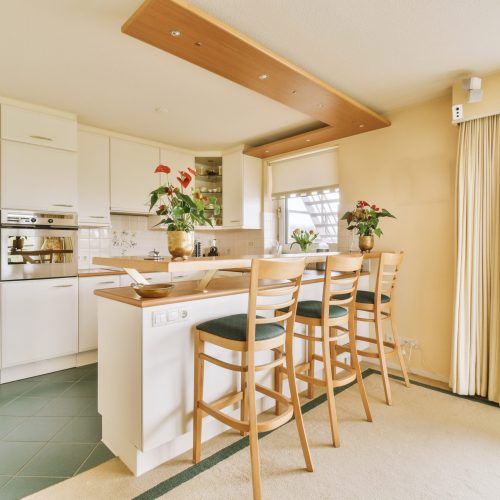 a kitchen with a bar and chairs and a window A beautifully lit kitchen, spacious and modern, accented by delicate flowers.