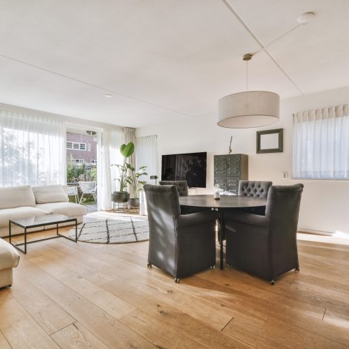 Comfortable armchairs and couch placed near lamps and shelf with TV and dining zone with kitchen against window in modern living room