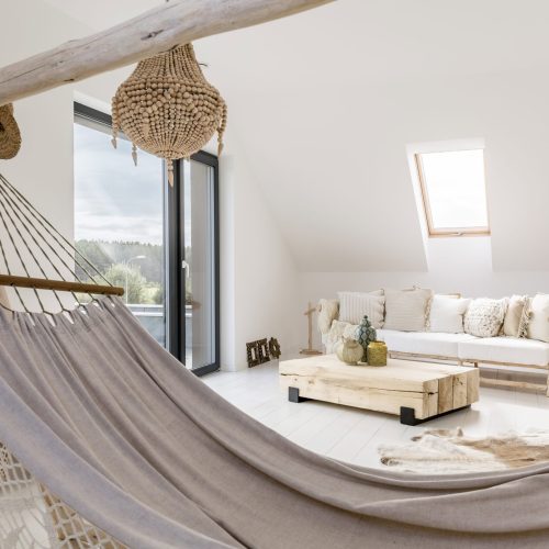 Grey handmade hammock standing in the white attic room with wooden sofa